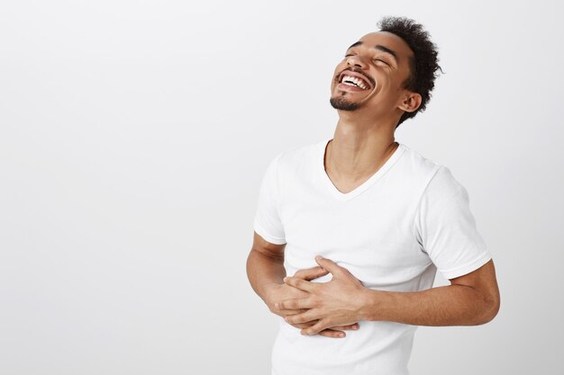 Uomo afroamericano spensierato che ride e sorride, ascolta uno scherzo divertente
