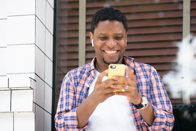 Uomo afroamericano utilizzando il suo telefono cellulare mentre era seduto alla vetrina di un negozio sulla strada. Concetto urbano.