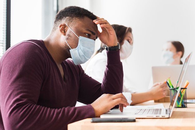 Uomo al lavoro in ufficio durante una pandemia con maschera facciale