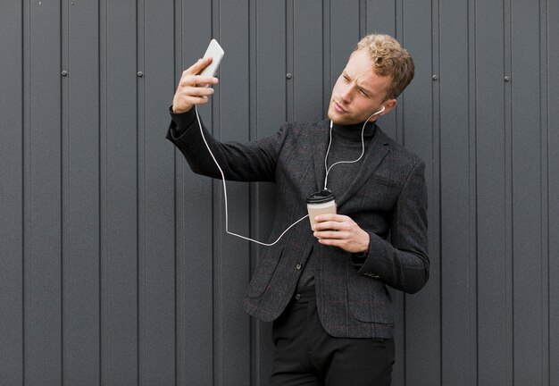 Uomo alla moda con caffè che prende un selfie