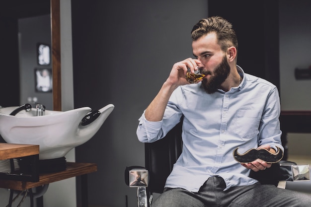 Uomo alla moda con drink nel negozio di barbiere