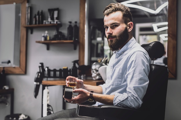 Uomo alla moda con la bevanda dell&#39;alcool nel negozio di barbiere