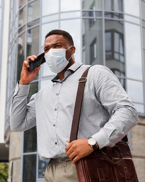 Uomo alla moda con la maschera mentre va al lavoro e parla al telefono durante la pandemia