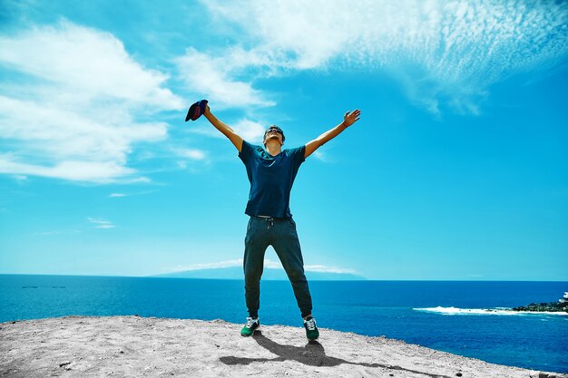 Uomo alla moda felice in abbigliamento casual che sta sulla scogliera della montagna