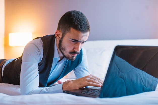 Uomo alla moda sul letto utilizzando il computer portatile