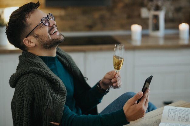 Uomo allegro che beve champagne pur avendo un appuntamento virtuale su uno smartphone a casa