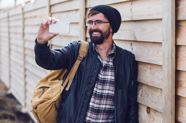 Uomo allegro della barba hipster che sorride e che fa autoritratto con il telefono cellulare