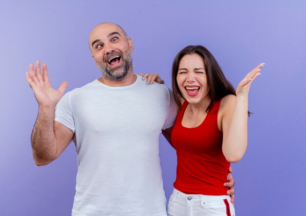 Uomo allegro delle coppie adulte che mostra la mano vuota con gli occhi incrociati e la donna infastidita che mette la mano sulla sua spalla e che mostra la mano vuota con gli occhi chiusi