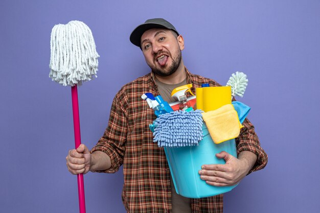 Uomo allegro delle pulizie che tiene in mano attrezzature per la pulizia e mop