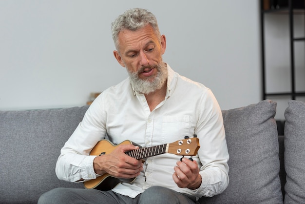 Uomo anziano a casa che suona l'ukulele sul divano