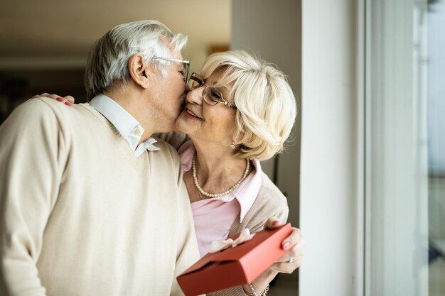 Uomo anziano che bacia il suo mentre riceve un regalo da lei a casa