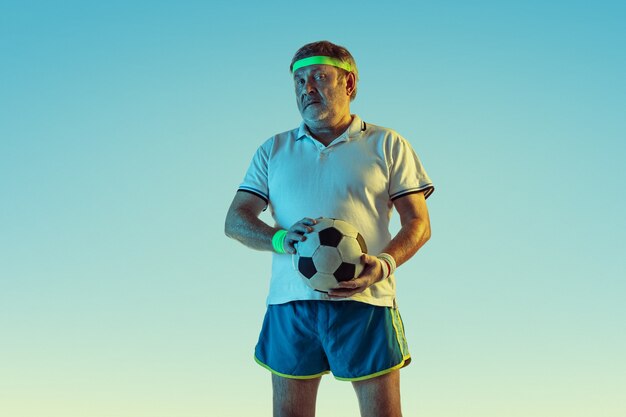 Uomo anziano che gioca a calcio in abbigliamento sportivo su sfondo sfumato e luce al neon