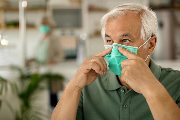 Uomo anziano che regola la maschera protettiva sul viso a causa dell'epidemia di coronavirus