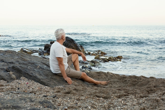 Uomo anziano che riposa in spiaggia e ammira l'oceano