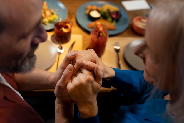 Uomo anziano che sorprende la sua amica e le tiene le mani in un ristorante