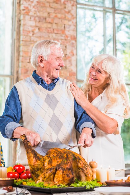 Uomo anziano che taglia pollo al forno al tavolo vicino alla donna
