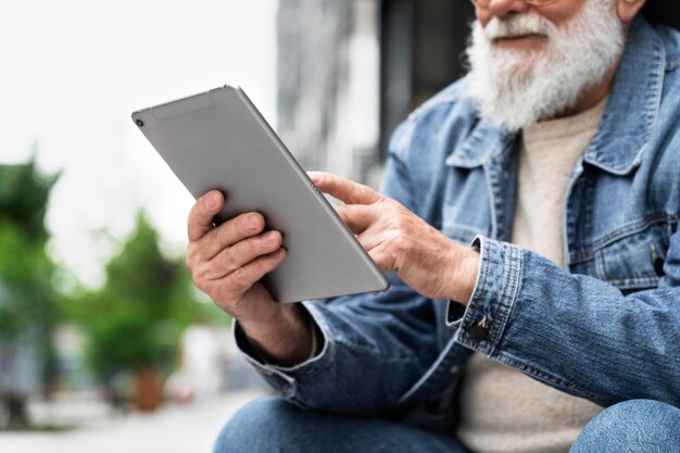 Uomo anziano che utilizza tablet all'aperto in città