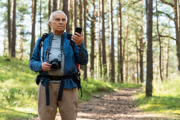 Uomo anziano che viaggia all'aperto con fotocamera e smartphone