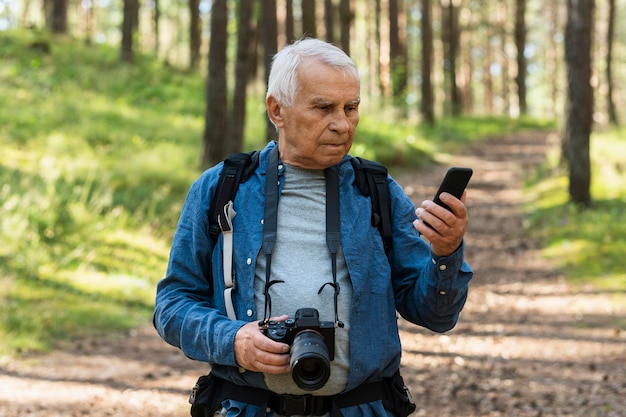 Uomo anziano che viaggia nella natura con fotocamera e smartphone