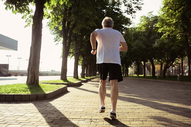 Uomo anziano come corridore con bracciale o fitness tracker in strada della città