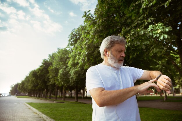 Uomo anziano come corridore con tracker di fitness in strada della città