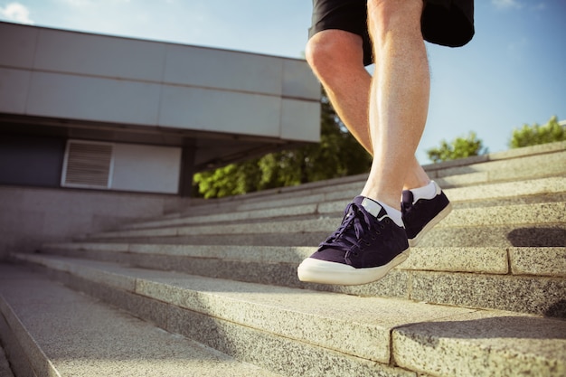 Uomo anziano come corridore in strada della città. Primo piano di gambe in scarpe da ginnastica. Modello maschio caucasico fare jogging e allenamento cardio nella mattina d'estate. Stile di vita sano, sport, concetto di attività.