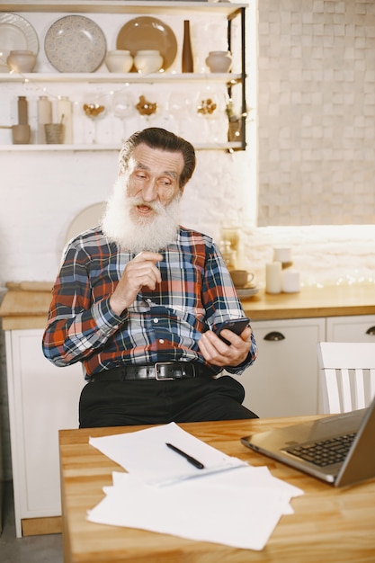 Uomo anziano con il computer portatile. Nonno seduto in un addobbo natalizio. Uomo con il cellulare.