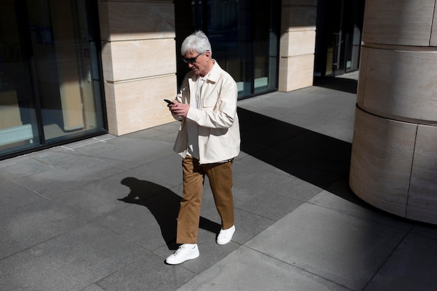 Uomo anziano con occhiali da sole all'aperto in città utilizzando lo smartphone mentre si beve un caffè