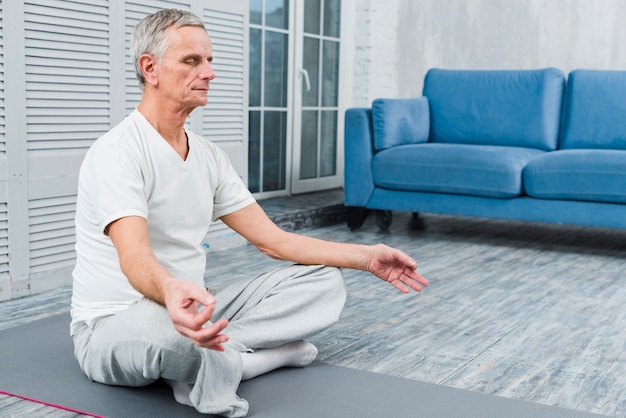Uomo anziano concentrato che medita su stuoia a casa