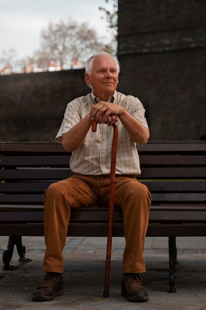 Uomo anziano del colpo pieno che si siede sul banco