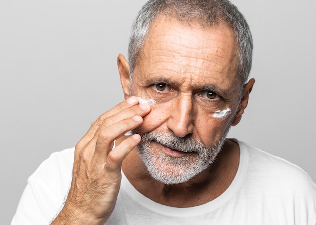 Uomo anziano del primo piano usando la crema per il viso