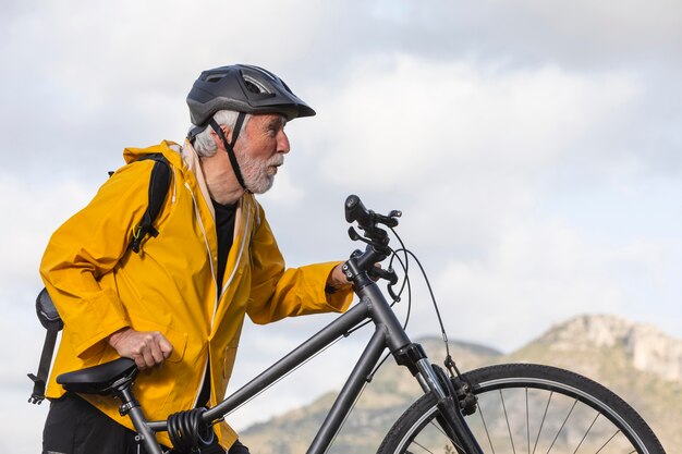 Uomo anziano del ritratto con la bici sulla montagna