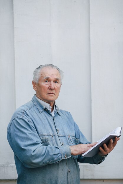 Uomo anziano elegante che sta sul fondo grigio con un libro