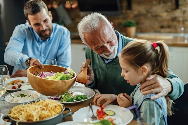 Uomo anziano felice che parla con sua nipote mentre pranza al tavolo da pranzo.