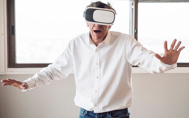 Uomo anziano in camicia bianca utilizzando una cuffia di realtà virtuale nella stanza