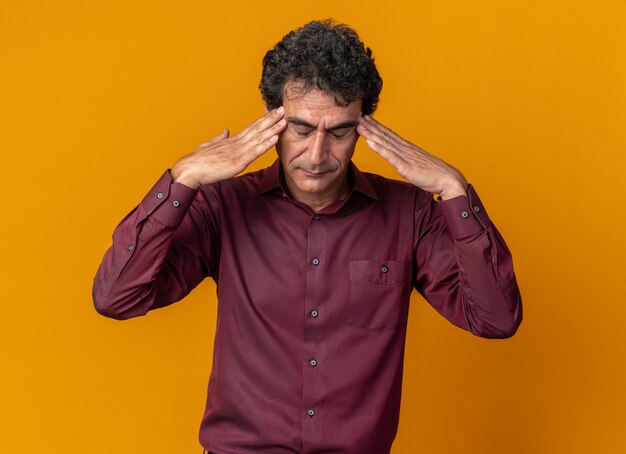 Uomo anziano in camicia viola che sembra indisposto a toccarsi la testa con mal di testa