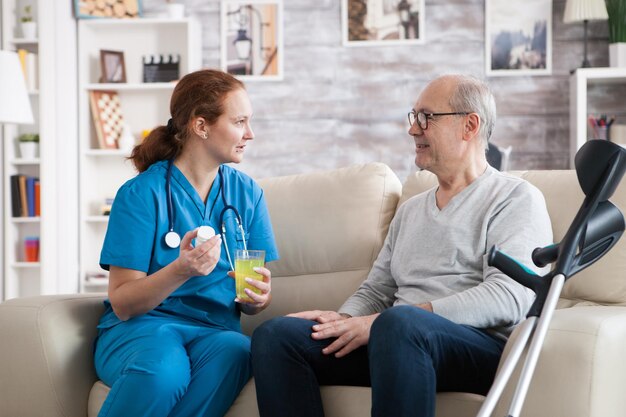 Uomo anziano in casa di cura che sorride all'infermiera mentre lei gli dà le pillole.