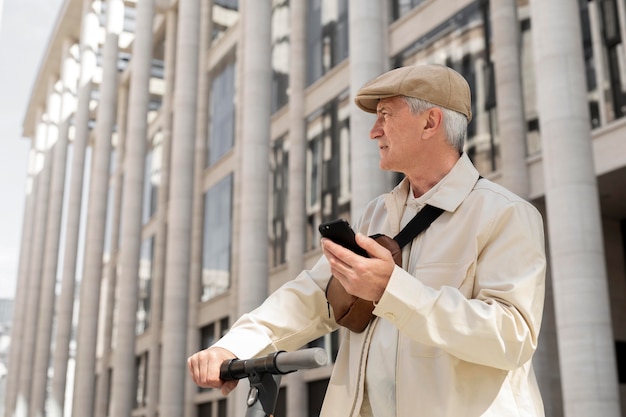 Uomo anziano in città con uno scooter elettrico che utilizza lo smartphone