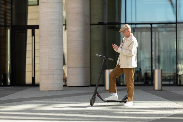 Uomo anziano in città con uno scooter elettrico che utilizza lo smartphone