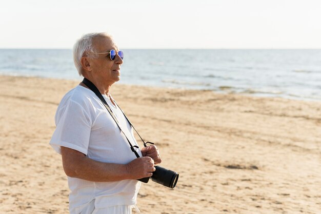 Uomo anziano in spiaggia con la macchina fotografica