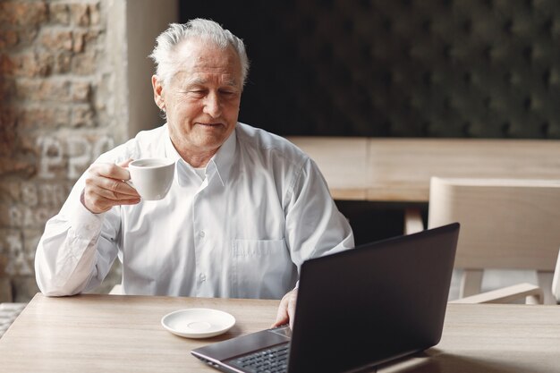 Uomo anziano seduto al tavolo e lavorare con un computer portatile