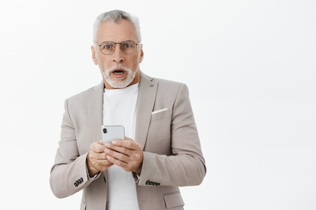 Uomo anziano senza fiato scioccato alla ricerca, utilizzando lo smartphone