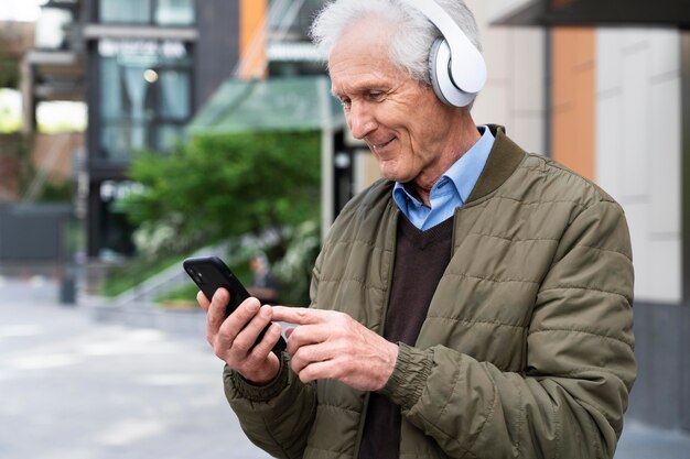 Uomo anziano sorridente in città che ascolta musica con le cuffie