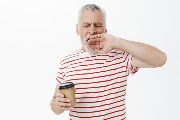 Uomo anziano stanco che sbadiglia assonnato, bevendo caffè