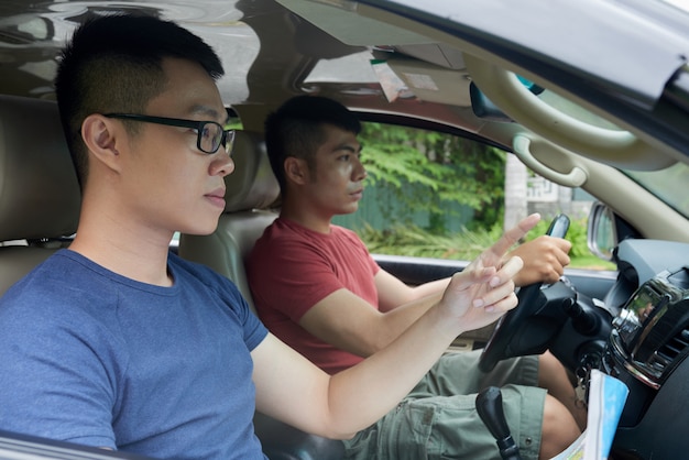 Uomo asiatico che conduce automobile ed amico con la mappa che indica in avanti