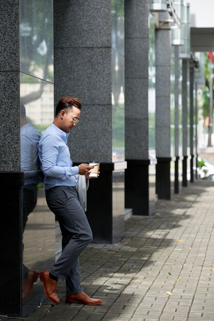 Uomo asiatico che ha pausa caffè all'aperto all'edificio per uffici