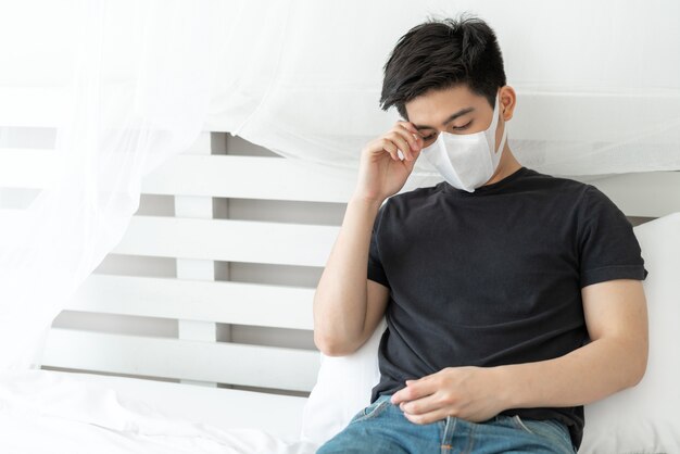 Uomo asiatico che indossa la maschera per il viso per proteggere la sensazione di mal di testa e tosse a causa del Coronavirus covid-19 nella stanza di quarantena