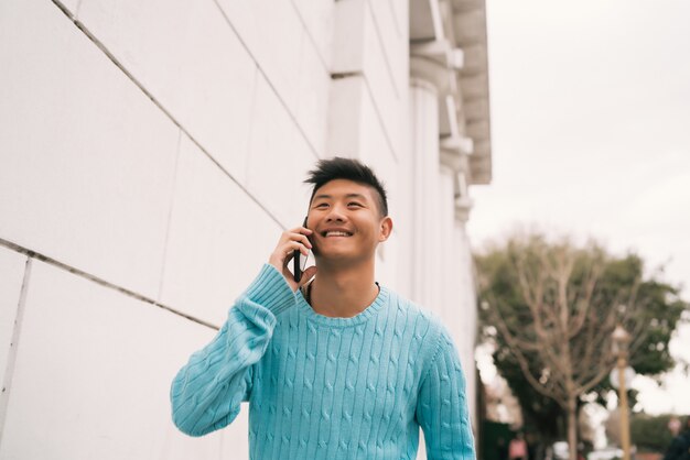 Uomo asiatico che parla al telefono all'aperto.