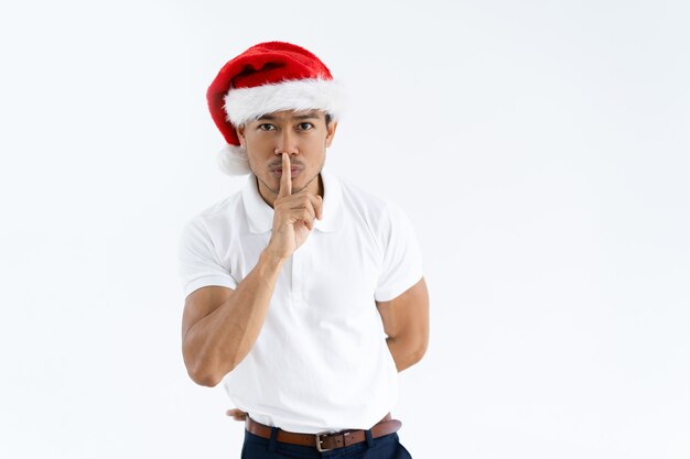 Uomo asiatico serio che porta il cappello di Santa e che fa gesto di silenzio