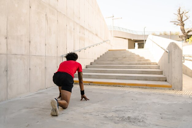 Uomo atletico afro pronto a correre all'aperto sulla strada